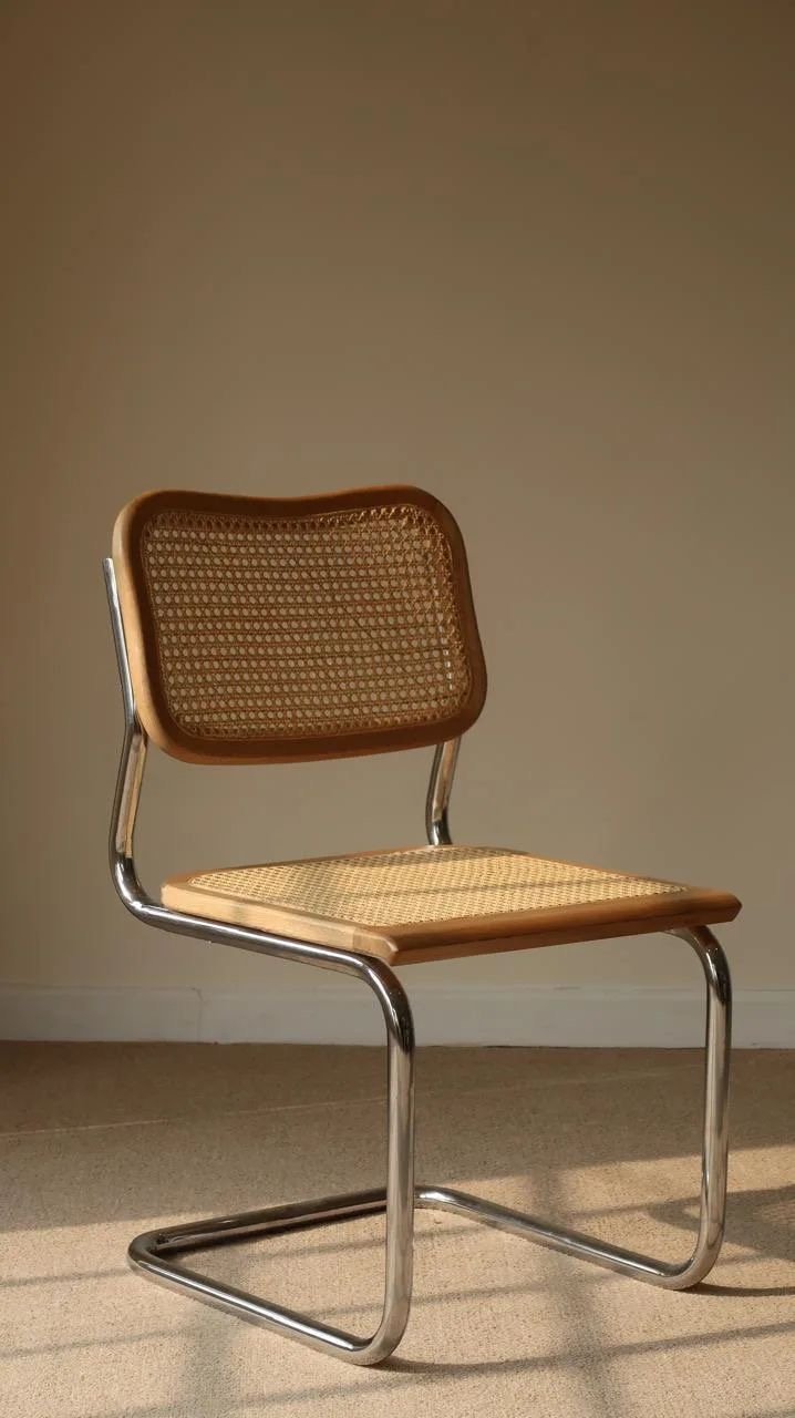 Cadeira Cesca, de Marcel Breuer, com estrutura em aço tubular cromado e assento e encosto de palhinha, num ambiente com luz lateral